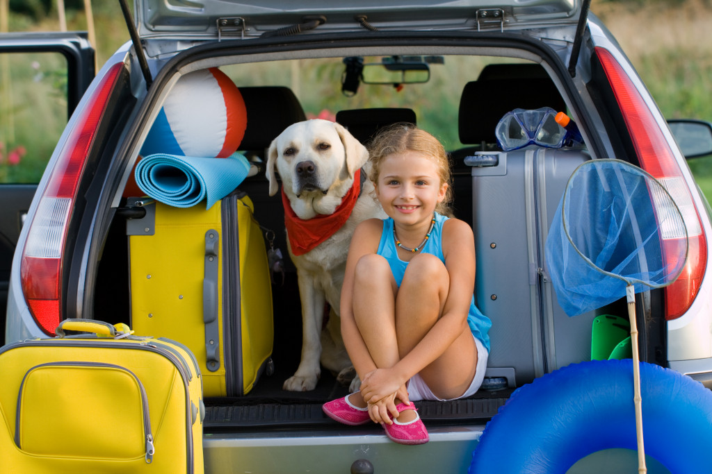 child sitting on a car's backseat storage with her dog