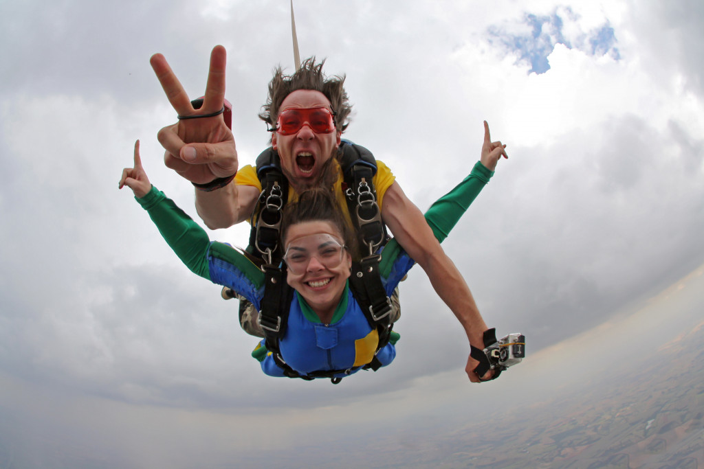 Two people strapped to each other while skydiving and posing to the camera