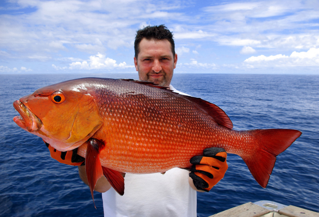 a man holding a large red snapper with his gloved hands near the sea