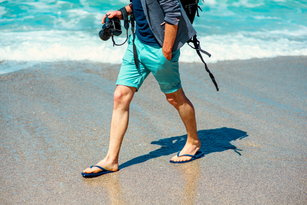 A man in shorts with a camera walking on the beach