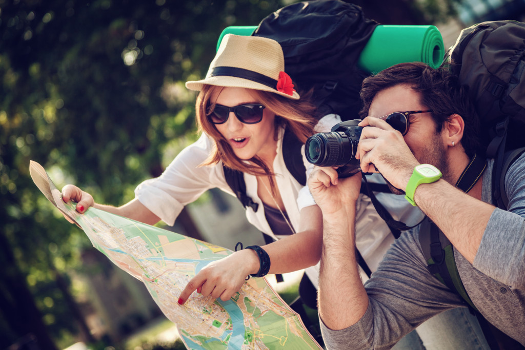 young male and female tourists using map and camera while sightseeing